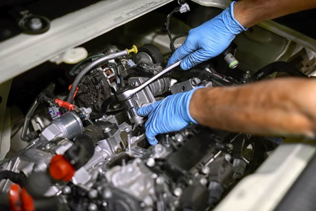 Mains gantées de bleu réparant un moteur de voiture. Un mécanicien utilise une clé à cliquet sur un composant moteur complexe.
